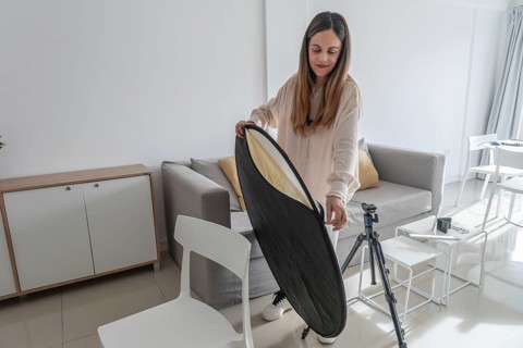 Woman standing and unfolding a collapsible gold and silver photography reflector beside a camera