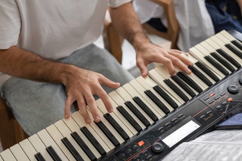A close-up of a mans hands playing a keyboard in a cozy home setting. The atmosphere is relaxed and