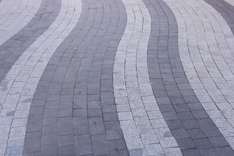 Curved lines of gray and white paving stones create an eye-catching pattern on an urban walkway.