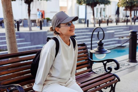 A cheerful middle-afed caucasian woman sits on a wooden bench, enjoying a sunny day in an outdoor