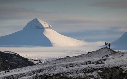 Two people, including a photographer with a stand in front of one of the three mountains Tee