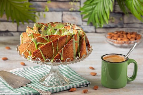 A cake with green icing next to a cup of coffee and almonds