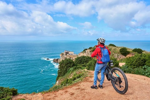 Attractive senior woman riding her electric mountain bike on the rocky cliffs of Nazare. western