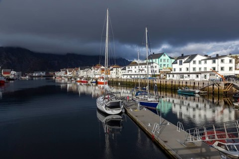 Picturesque harbor with sailboats and traditional wooden houses under dramatic cloudy skies,