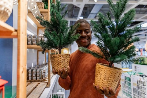 A person is in a store looking at a small Christmas tree. They smile while holding it. The store is