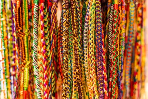 Colorful woven bracelets hang in a display. The intricate patterns feature various bright colors,