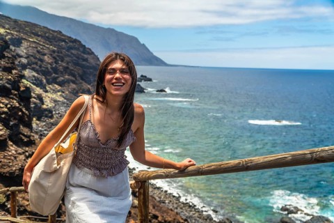 Young woman smiling while standing on a coastal path overlooking the atlantic ocean, exploring the
