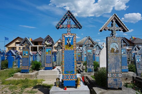 Traditionally painted wooden crosses in the Romanian Sapân?a cemetery under bright skies,