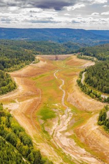 Aerial view of an empty riverbed with adjacent forest and cloudy sky, rehabilitation of