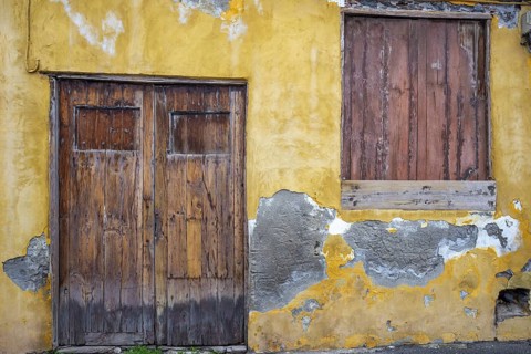 Weathered façade of an empty house in Garachico, characterized by crumbling plaster and old wooden