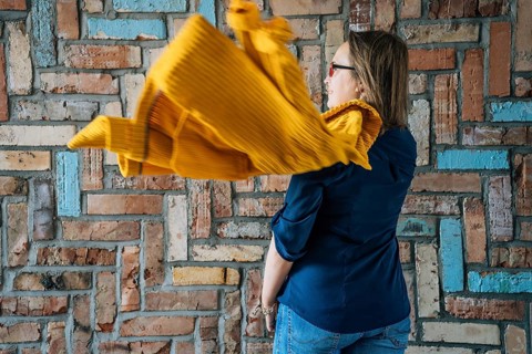 Rear view of a 40-year-old woman in glasses with a flying yellow jacket against a colorful brick