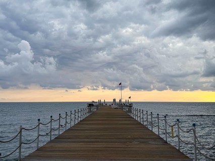 A wooden dock with railing leads into the sea as storm clouds gather in the sky, Side, Manavgat,