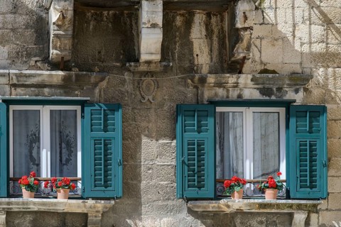 Windows with lace curtains, teal shutters and red geraniums, in a historical building, Trogir,