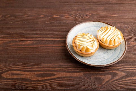 French lemon tart with meringue on brown wooden background, side view, copy space