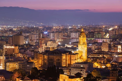 Telephoto blue-hour view of illuminated Malaga Cathedral in Spain, rising above the historic center