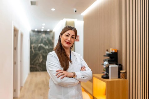 Woman doctor wearing a lab coat and smiling, standing with arms crossed in a reception area or
