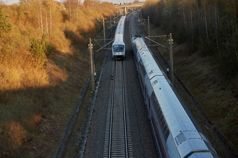 Train traveling through a scenic railway corridor at sunset, surrounded by trees and overhead power