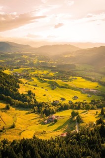 Sun-drenched landscape with scattered houses and meadows in a mountainous forest area, Oberstaufen