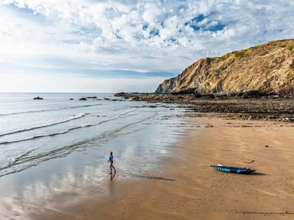 Woman and dog with kayak on Beach from a drone, North Devon and Cornwall Coastpath Border from a