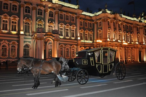 Historic carriage with horses in front of an impressively illuminated palace at night, Winter