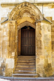 A weathered stone doorway with a moulded pointed arch and carved spandrels frames a dark panelled
