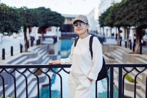 Middle-aged woman stands casually by a railing, smiling while overlooking a serene water feature in