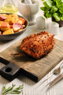 Roasted turkey breast on wooden cutting board in kitchen. Nearby bowl with vegetables. Oil and