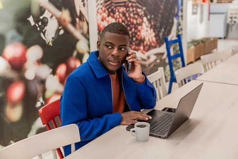 Young African man using a laptop and smartphone in a modern cafe. Bright interior with decorative
