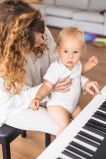 A mother lovingly holds her baby at the piano, engaging in a nurturing interaction