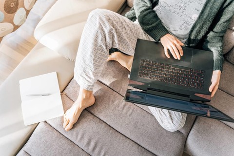 A woman in home clothes with a laptop, next to her is a notebook and a pen, Person working on a