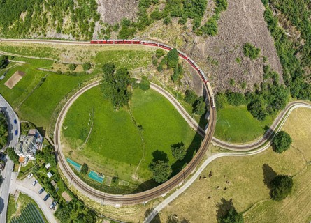 Red train of the Rhaetian railroad line, Bernina Express, passing the circular Brusio viaduct,