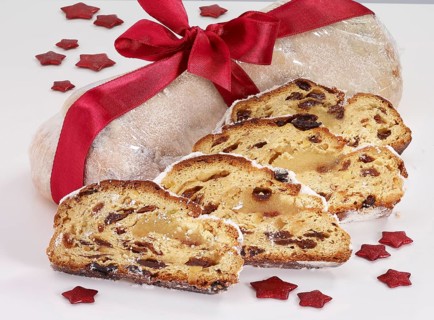 Christmas stollen wrapped and decorated with red ribbon, in front of 4 slices of stollen, red stars