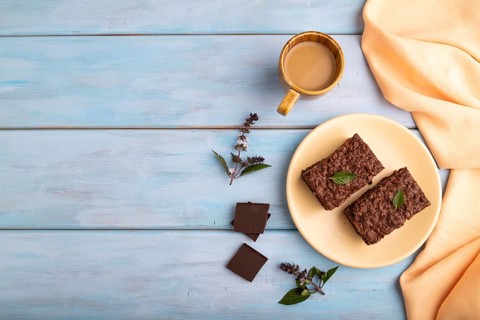 Chocolate cheese cake with cup of coffee on blue wooden background with orange textile, copy space,