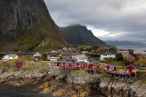 Picturesque fishing village Hamnøy with red Rorbuer huts on rocky cliffs against steep mountain