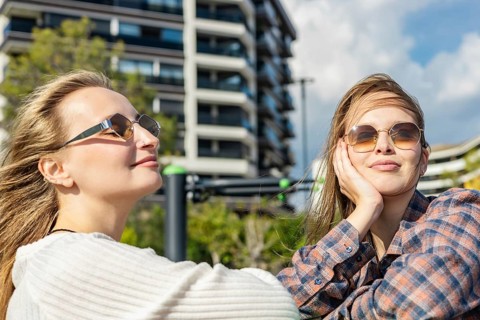 Two young women enjoying a sunny day outdoors. One has long blond hair and wears sunglasses. The