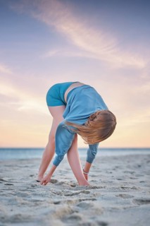 Beach scene featuring a woman, yoga, prasarita padottanasana, wide leg fold, forward bend, and