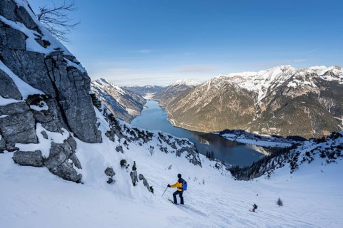 Picturesque view of Achensee and wintry mountain scenery, ski tourers descending from the summit of