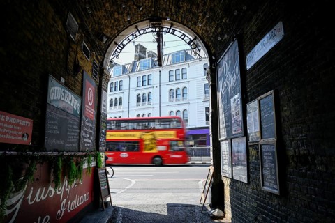 View through the archway of a historic pub onto a passing red double-decker bus, near London Bridge