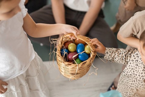 Two young girls holding a woven basket filled with colorful eggs. The scene captures a joyful