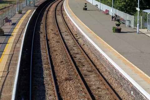 Person sitting on platform bench waiting for train, oblique overhead view of railways tracks,