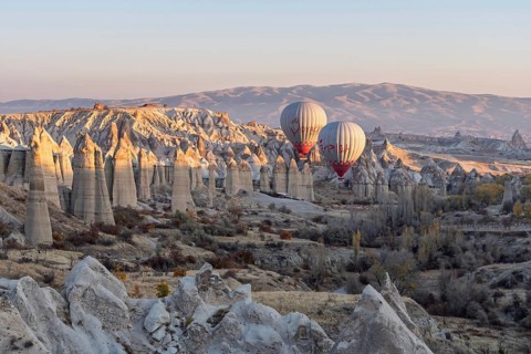 Hot air balloons float over a picturesque rocky landscape in soft morning light, Cappadocia, Turkey
