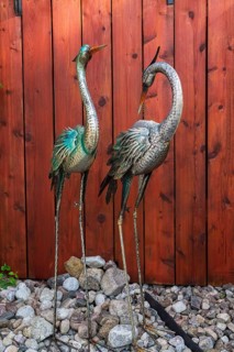 Grey, turquoise painted metal ornamental waterbird sculptures in loose stones border against