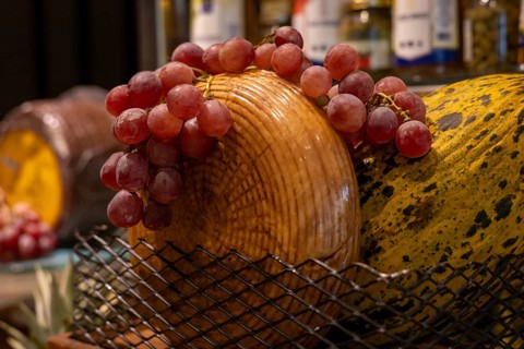 A basket filled with fresh red grapes sits atop a wooden cheese board. The cozy atmosphere enhances