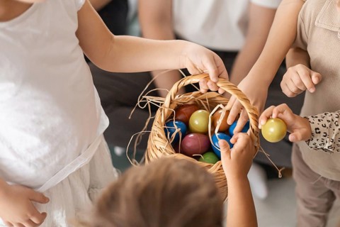 Children gather around a basket filled with colorful eggs. The scene captures a joyful family