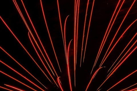 Orange and red illuminated trailing streaks of fireworks in black sky at night in summer, Quebec,