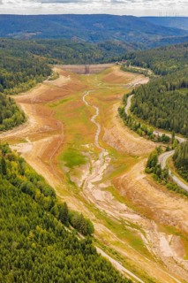 Aerial view of a dry riverbed surrounded by dense forests and hills, rehabilitation of the