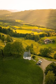 Aerial view of picturesque hilly landscape with small chapel in sunlight, Bruder Klaus chapel,