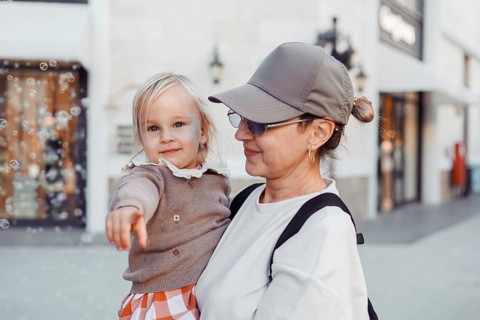 A little girl playfully points towards bubbles while being held by her smiling grandmother. They