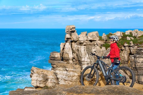 Senior woman riding her electric mountain bike on the rocky cliffs of Peniche at the western