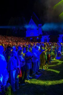 Open-air concert at night with blue lighting and Gothic architecture in the background, Calwer